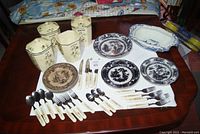 Full view of assorted old china pieces including the canister set with floral designs, various plates, and the cutlery set.