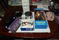 Wide photo showing multiple boxed items including the Polaroid Spectra 2 camera, Can-Pro handleset in retail packaging, and other items spread on a wooden table.