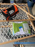 Orange and black pet harness, wooden foldable pet gate, and green and white pet blanket on a white grid surface