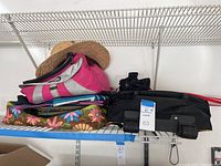 Shelf with pink and gray duffle bag, black travel bag, floral print cooler bag with lime green accents, and straw beach hat