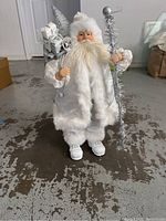 Front view of Winter Wonderland Santa wearing white and silver trim coat, holding gift bag and silver staff.
