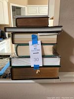 Stack of assorted hardcover books with one blue label tape marked '30' on top book.