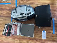 Overview showing Memorex boombox, two CD cases, mixed cassettes and CDs on wooden floor.