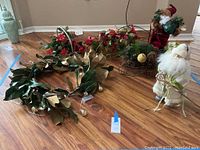 Christmas decor items including two Santa figurines, wreath, floral baskets, and a decorative sleigh arranged on floor.
