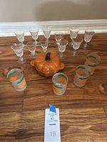 Clear glass cordial glasses arranged behind pumpkin dish and frosted glasses with orange detail.