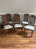 Full set of six wooden dining chairs arranged together on hardwood floor showing caned backs and striped upholstered seats.
