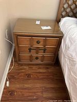 Full view of wooden Drexel nightstand showing 3 drawers and glass top beside bed on wood floor.