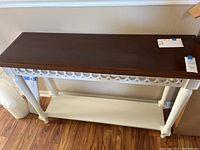 Full view of the wooden table showing the cherry top and white legs with decorative trim and lower shelf