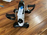 Top angled view showing pedals, foot straps, central resistance knob, and calorie display with attached label.