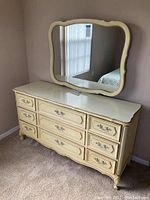 Full view of Henry Link dresser with mirror in a bedroom showing cream distressed finish and ornate drawer handles.