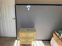 Nightstand placed in front of full box spring; parts of other furniture visible
