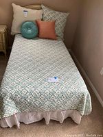 Twin bed made with floral quilt bedding and assorted pillows, placed in an upstairs bedroom corner.