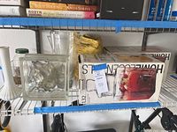 Two Home Essentials glass beverage dispensers on shelf with box, surrounded by additional glass vessels and cleaning cloth.