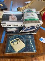 Photo of Rowenta steam iron box, AriJoi air purifying bag package, and Midland weather radio box on a table.