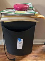 Photo of black paper shredder filled with assorted paper and folders on top