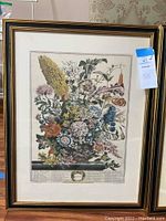Full view of one floral framed print showing intricate flowers and black frame with gold trim.