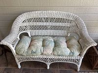 Close-up of the white wicker love seat with green floral cushions showing paint chipping.