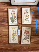 Four framed floral prints by Ray Harm laid on wooden floor, each depicting different flowers in detailed botanical style with muted background.