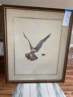 Full view of framed Ray Harm Kestrel Falco Sparverius print showing the bird in mid-flight with prey insect, in wooden frame with beige mat.