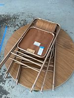 Three Samsonite folding chairs stacked on top of a round folding table with faux wood finish.