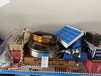 Photo showing Shark Mini Vac handheld vacuum, Safe Guide Cutter box, amber glass ashtray, playing cards, and other items on metal shelf