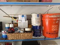 Shelf with assorted paint cans, spray cans, tools, lightbulbs, and flashlights in a basket