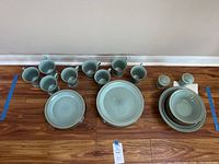 Full set of teal stoneware items arranged, including eight mugs, eight dinner plates, eight salad plates, a large serving bowl, and salt and pepper shakers.