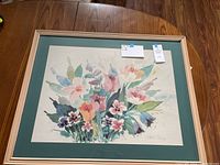 Full view of framed watercolor painting showing colorful floral arrangement in cream-colored frame with green matte.