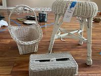 White wicker basket, stool, and tissue cover displayed on wooden floor.