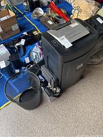 Photo showing Royal 184MX shredder, black plastic trash can, and scattered office supplies including power cords and camera accessories.