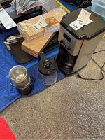 Overview showing the coffee maker, extra glass carafe, KitchenAid grinder, and pack of coffee filters on a carpeted surface with a blue cloth beneath.