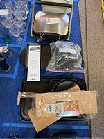 Photo of Raclette grill, cookware pans, cedar planks packaged in plastic, and Cheeseboard grill on blue padded surface.