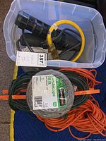 Contents of a plastic bin with various power strips, electrical cords, a yellow converter cable, and a labelled coiled green outdoor extension cable.