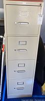 Front view of the beige metal filing cabinet with four drawers and metal handles.