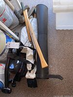 Photo showing several wooden-handle garden tools and a black plastic tube accessory alongside a white carrying bag on floor.