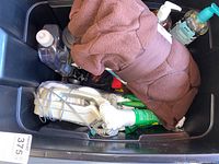 Plastic bin containing various emergency supplies: brown towel, hand sanitizers, white rope, flashlight, and other items.