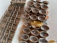 Close-up of metal bracelets showing rectangular grid pattern and oval/teardrop-shaped links with oxidation and patina, as well as yellow gold-tone rhinestone hoop earrings.