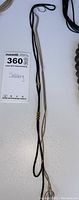 Photo showing the full length of the black cord necklace with gold-tone accents and a silver pendant.