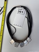 Full view of silver beaded necklace with multiple black cord strands and magnetic clasp alongside measuring tape showing length.