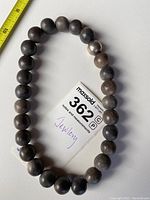 Stone beaded necklace laid flat to show bead color and size; beads are smooth and round in natural earth tones including shades of gray and brown.