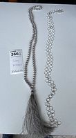 Full view of two long necklaces: one white cloth beaded with tassel, one silver circular link chain.