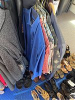 Men's clothing rack showing various button shirts including Hawaiian styles and two suits, placed above shoes.