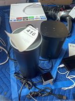 Image showing both speakers, power cable, and power adapter for the Amazon Alexa speaker, alongside other items in the background.