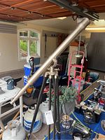 Telescope mounted on tripod standing upright in garage with various items around.
