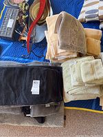 Top view of several folded bath towels in beige, black, and light green colors arranged on a blue protective covering.