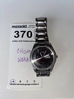 Front view of Citizen men's wristwatch showing silver band and black dial with day and date display.