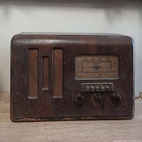 Front view of wooden antique Marconi tube radio with speaker grille and control knobs