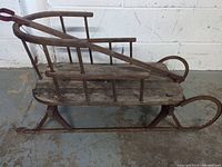 Side view of antique wooden sled showing slatted seat, side rails, and metal runners with wear.