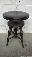 Front angled view showing the round adjustable seat and turned legs with claw feet, placed against a blank wall.