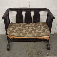 Front view of antique wooden bench showing carved backrest and floral cushions on seat.